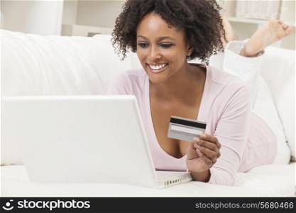 A beautiful happy mixed race African American girl or young woman laying down on sofa using a laptop computer shopping on line using her credit card