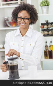 A beautiful happy mixed race African American girl or young woman making coffee with a cafetiere in her kitchen at home