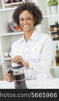 A beautiful happy mixed race African American girl or young woman making coffee with a cafetiere in her kitchen at home