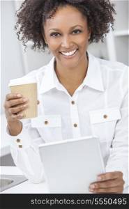 A beautiful happy mixed race African American girl or young woman using a tablet computer in her kitchen drinking coffee