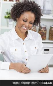 A beautiful happy mixed race African American girl or young woman using a tablet computer in her kitchen