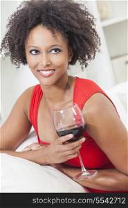 A beautiful happy mixed race African American girl or young woman wearing a red dress and drinking red wine at home