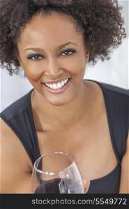 A beautiful happy mixed race African American girl or young woman wearing a black dress and drinking red wine at home