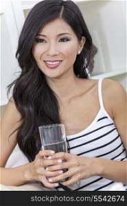 A beautiful happy young Chinese Asian Oriental woman with a wonderful toothy smile drinking a glass of water at home