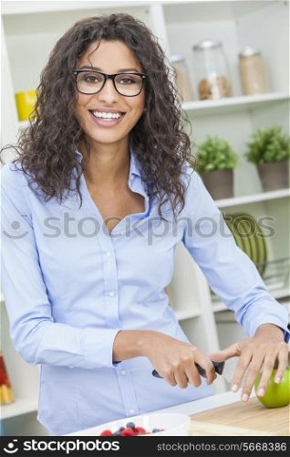 A beautiful happy young woman or girl wearing glasses cutting &amp; preparing an apple for fresh fruit salad food in her kitchen at home