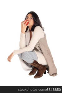 A beautiful Hispanic woman eating a red apple, crouching on the floor, isolated for white background.