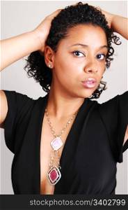 A beautiful Hispanic woman standing in the studio for a portrait with herblack curly hair, in a black dress and nice necklace, light gray background.