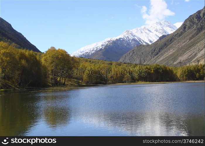 A beautiful lake with yellow trees on the beach and snow-capped peaks in the distance