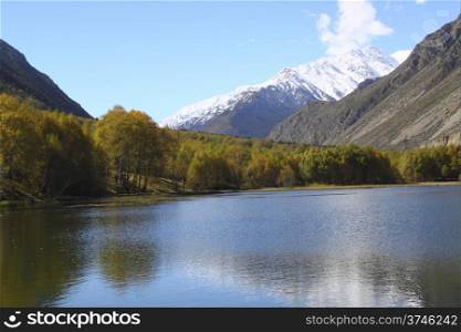 A beautiful lake with yellow trees on the beach and snow-capped peaks in the distance