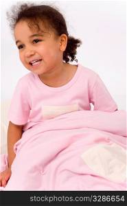 A beautiful little mixed race girl dressed in pink pajamas, sitting up in bed and smiling