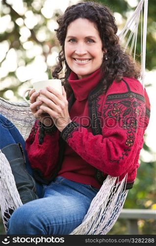 A beautiful mature woman sitting on a hammock drinking coffee
