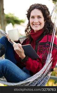 A beautiful mature woman sitting on a hammock reading a book