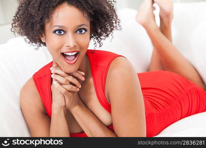 A beautiful mixed race African American girl or young woman laying down wearing a red dress looking happy and surprised