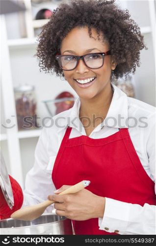 A beautiful mixed race African American girl or young woman looking happy wearing geek glasses a red apron &amp; cooking in her kitchen at home