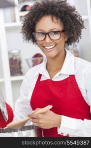 A beautiful mixed race African American girl or young woman looking happy wearing geek glasses a red apron &amp; cooking in her kitchen at home