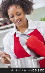 A beautiful mixed race African American girl or young woman looking happy wearing red apron &amp; cooking in her kitchen at home