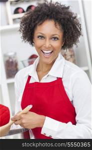 A beautiful mixed race African American girl or young woman looking happy wearing a red apron &amp; cooking in her kitchen at home