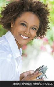 A beautiful mixed race African American girl or young woman looking happy taking pictures or photographs outside with a retro digital camera