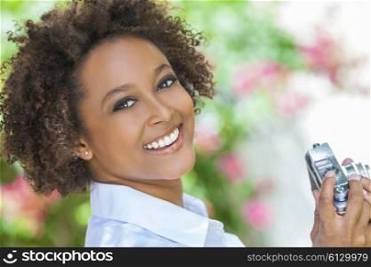 A beautiful mixed race African American girl or young woman looking happy taking pictures or photographs outside with a retro digital camera