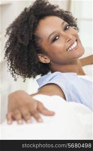 A beautiful mixed race African American girl or young woman sitting on sofa at home looking happy and relaxed