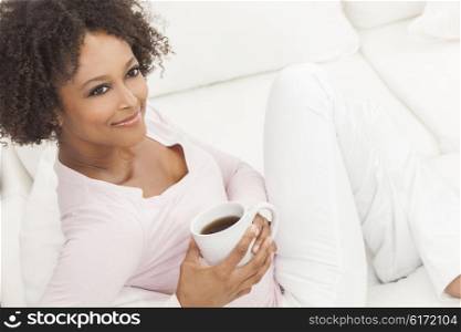 A beautiful mixed race African American girl or young woman sitting on sofa at home looking happy and relaxed drinking cup of tea or coffee