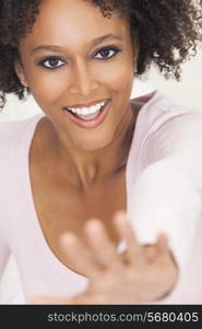 A beautiful mixed race African American girl or young woman with perfect teeth, looking happy and smiling reaching hand out towards camera