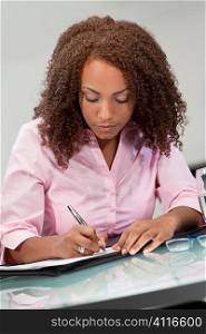 A beautiful mixed race African American girl, student or businesswoman sitting at a desk and writing.