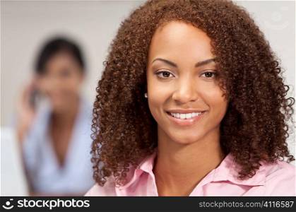 A beautiful mixed race African American girl with perfect teeth and smile behind her out of focus is an Asian girl talking on the phone