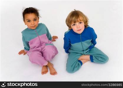A beautiful mixed race little girl and a blonde boy dressed in sleep suits look up into the camera