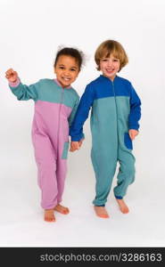 A beautiful mixed race little girl and a cute blonde boy dressed in sleep suits holding hands, laughing and having fun together