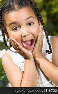 A beautiful mixed race little girl hands up to her face and expressing happy surprise. The shot is taken in natural summer sunshine.