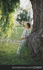 A beautiful portrait of a pregnant girl near a fallen branch of a weeping willow tree.. Portrait of a girl at the trunk of a weeping willow 1729.