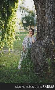 A beautiful portrait of a pregnant girl near a fallen branch of a weeping willow tree.. Portrait of a girl at the trunk of a weeping willow 1730.