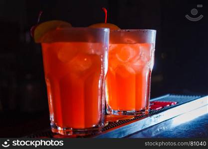 A beautiful red cocktails with slice of orange and cherry in a tall glasses. close-up