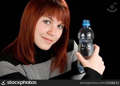 A beautiful redhead girl holding a bottle of water in her hand and looking at the camera. Studio shot.