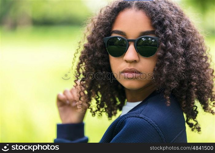 A beautiful sad moody mixed race African American female girl child teenager young woman in sunshine wearing sunglasses with attitude