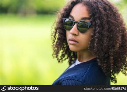 A beautiful sad moody mixed race African American female girl child teenager young woman in sunshine wearing sunglasses with attitude