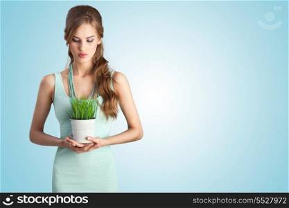 A beautiful sensual girl in white dress holding a flower pot of decorative lawn grass.