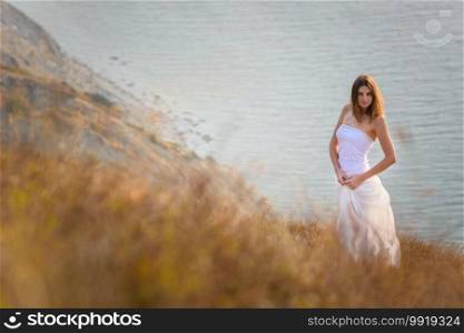 A beautiful slender girl stands on a hillock against the background of the sea