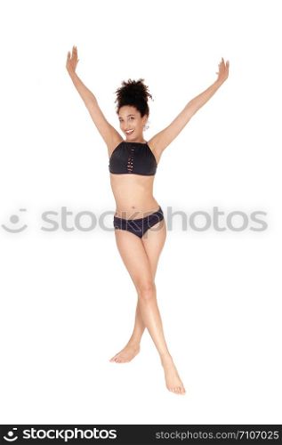 A beautiful slim young multi-racial woman standing in a black bikini in the studio lifting booths arms, bare foot with her curly black hair in abun on her head, isolated for white background