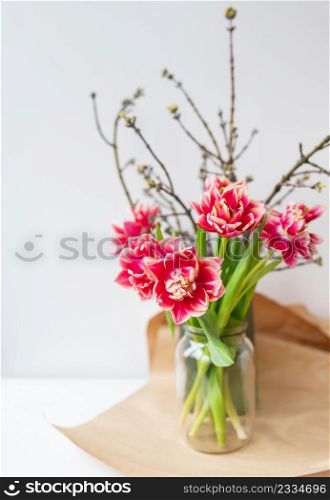 A beautiful spring bouquet of tulips stands in a vase along with spring branches. Surprise concept, birthday. Vertical photo, place for an inscription. A beautiful spring bouquet of tulips stands in a vase along with spring branches. Surprise concept, birthday. Vertical photo, place for an inscription.