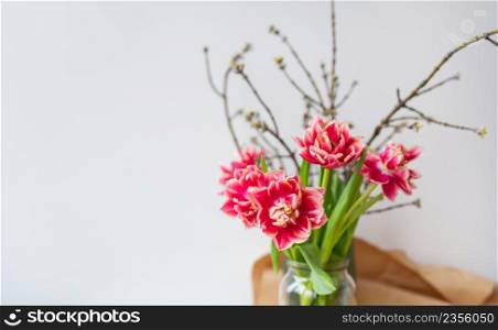 A beautiful spring bouquet of tulips stands in a vase along with spring branches. Surprise concept, birthday. Place for an inscription. A beautiful spring bouquet of tulips stands in a vase along with spring branches. Surprise concept, birthday. Place for an inscription.