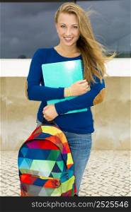 A beautiful student in the college holding a backpak and notebooks