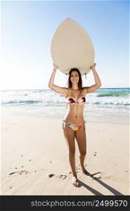 A beautiful surfer girl at the beach holding up her surfboard