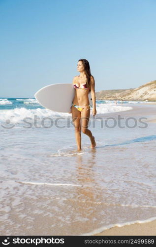 A beautiful surfer girl at the beach holding up her surfboard