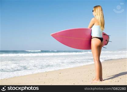 A beautiful surfer girl looking at the beach with her surfboard