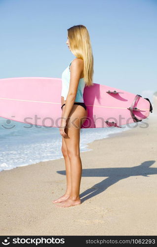 A beautiful surfer girl looking at the beach with her surfboard