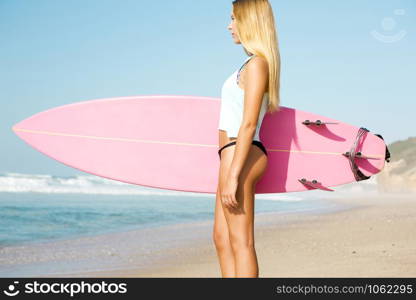 A beautiful surfer girl looking at the beach with her surfboard