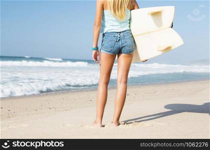A beautiful surfer girl walking at the beach with her surfboard