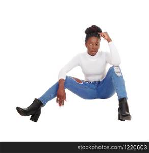 A beautiful tall African American woman sitting in jeans and white top on the floor in the studio, isolated for white background